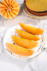 Fresh Sliced Cantaloupe Melon on White Plate with Whole Fruit in Wicker Basket on Marble Counter