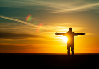 Uplifting freedom posture of a silhouette with open arms in golden light facing the horizon, a visual of gratitude and optimism for wellness campaigns
