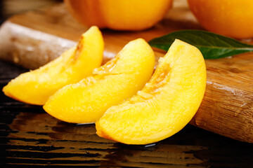 Freshly sliced ripe peaches on wooden cutting board with whole fruits in kitchen setting
