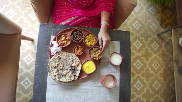 Young woman enjoying indian vegetarian spicy food platter or Rajasthani thaali with lots of delicious dishes. Complete meal. Female eating in eco friendly clay plate and bowls. Culture of india.