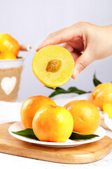 Fresh Golden Peach Slice in Hand with Whole Ripe Peaches on Wooden Board - Healthy Summer Fruit