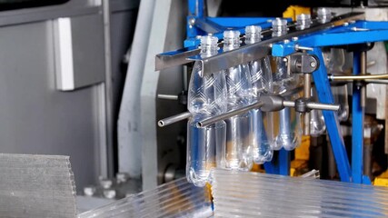 Clear plastic bottles are being gathered and positioned on a production line. The process demonstrates the efficiency of modern manufacturing techniques in a factory setting.