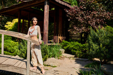 Elegant young Indian woman enjoying summer in a lush outdoor garden setting with wooden bridge