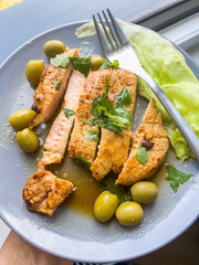 Sliced roasted pork with green olives served on a gray plate with a fork on the side, homemade meal.