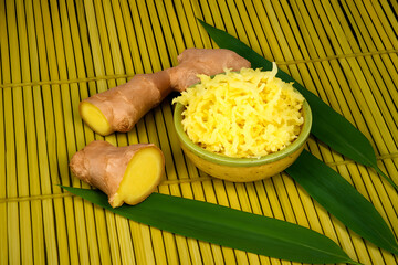 Fresh ginger root with grated ginger in bowl and bamboo leaves aromatic spice healthy cooking ingredient concept