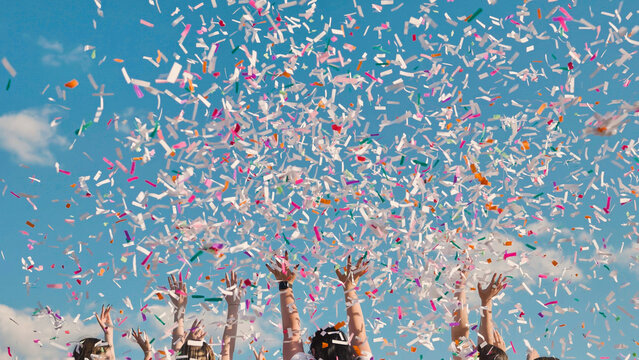 High school graduates celebrate by tossing colorful confetti into the sky against a backdrop of blue