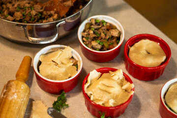 Assembling homemade turkey pot pies in red ramekins