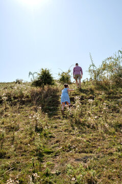 Father and daughter climbing a hill under bright summer sky.