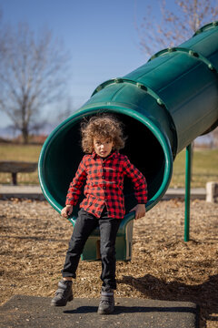 Child in red plaid shirt exits green playground slide