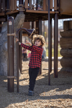 Child in red plaid shirt points while playing at playground tube