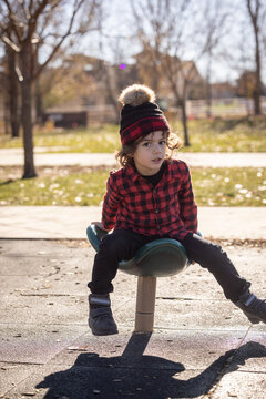 Child in red plaid shirt spins on playground toy in sunny park