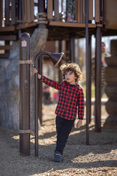 Child in red plaid shirt plays with speaking tube at playground