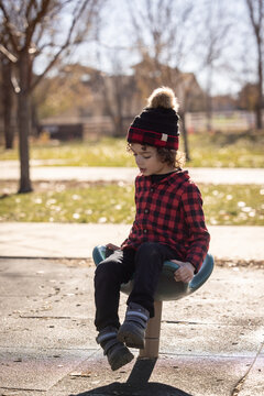 Child in red plaid shirt sits on playground spinner in autumn park