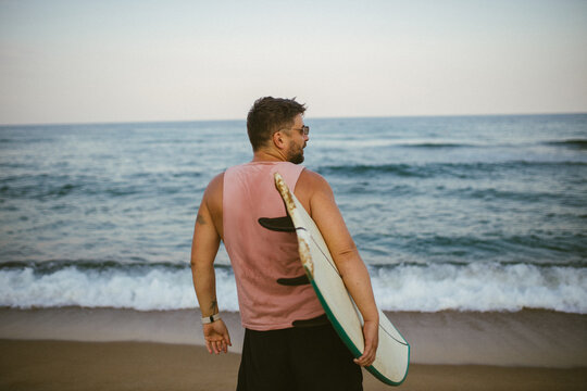 Man carrying surfboard on beach near ocean