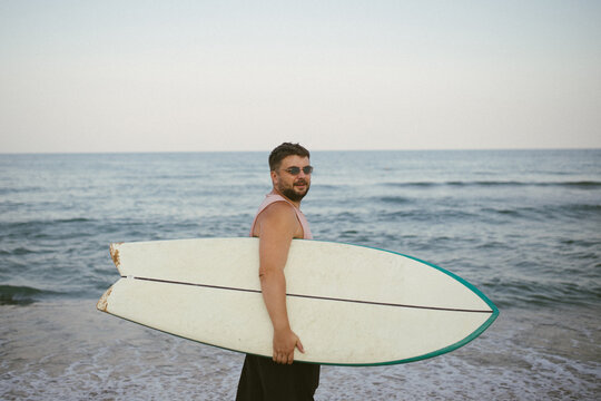 Man with surfboard looking back on beach by the sea