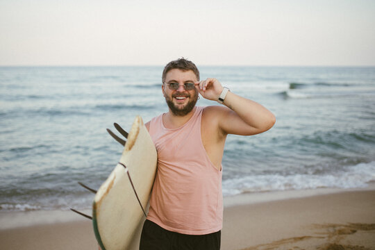 Man with surfboard looking back on beach by the sea