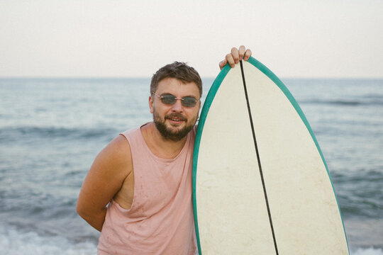 Man with surfboard looking back on beach by the sea