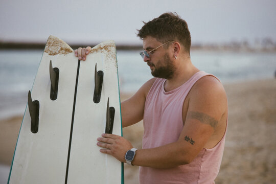 Man with surfboard looking back on beach by the sea