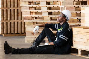 African American male worker in safety gear takes break while sitting on warehouse floor,...