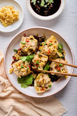 Delicious shrimp dumplings topped with spicy black sauce, fresh chili, coriander and minced garlic, fried and served with wooden chopsticks, ready to eat.