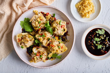 Delicious shrimp dumplings topped with spicy black sauce, fresh chili, coriander and fried minced garlic, ready to eat.