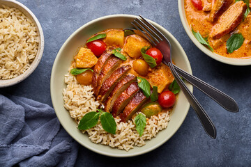 Tender roast duck in a delicious red curry with potatoes and tomatoes on brown rice and a bowl of roast duck red curry.