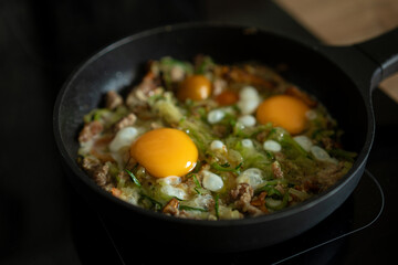 Cooking a vegetable and egg dish in a skillet with fresh ingredients on a stovetop in a cozy kitchen