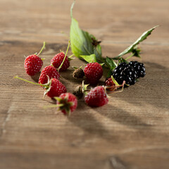 Fresh raspberries and blackberries arranged on a wooden surface with leaves showcasing vibrant colors and textures