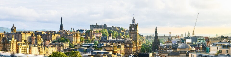 Fototapeta premium Panorama von Edinburgh bei Sonnenuntergang vom Calton Hill mit Blick auf Balmoral Hotel, Scott Monument, St Giles’ Cathedral, Tolbooth Kirk und Edinburgh Castle unter bewölktem Himmel in goldenem Lich