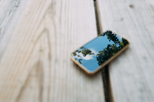 Smartphone on picnic table reflecting sky and trees