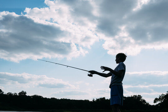 Silhouette of boy fishing against blue sky
