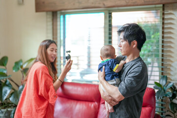 Obraz premium A man is holding a baby in his arms while a woman takes a picture of them. The scene is casual and relaxed, with the man and woman enjoying their time together
