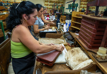 Skilled female workers rolling premium cigars by hand, carefully crafting tobacco products in...