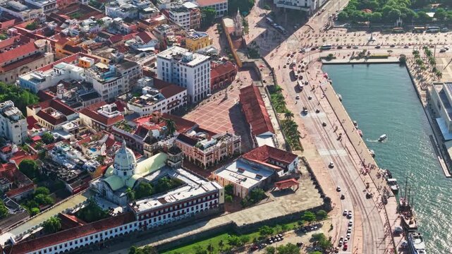 Slow motion tilt up drone video at sunset over Cartagena de Indias, Colombia, captures the vibrant Plaza del Reloj, Plaza de la Aduana, and city&rsquo;s dynamic traffic in golden light.