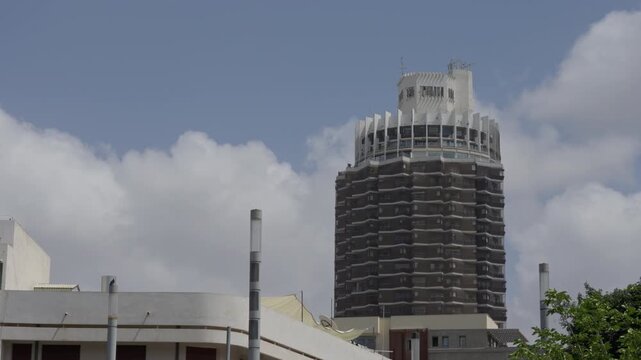 Tall building in Dizengoff, Tel Aviv, Israel with lower building in foreground. Blue skies with clouds. Bird flying. Wide shot. Slight pan right.