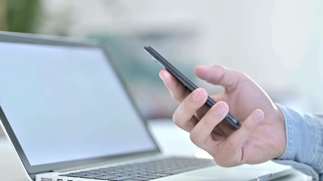 Business Person Scrolling news on smartphone closeup macro during workday office time on desk work laptop background