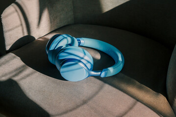 Wireless blue headphones illuminated by the sun rays are lying on a chair.