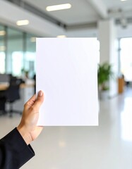 Hand holding a blank A4 paper sheet with space for text or mockups, against a modern office background. Copy space for business, education, or creative use