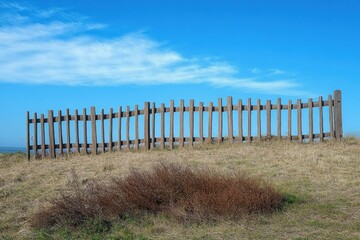 Old wooden fence on dry grassy hill under clear blue sky with gentle clouds evoking calm and openness