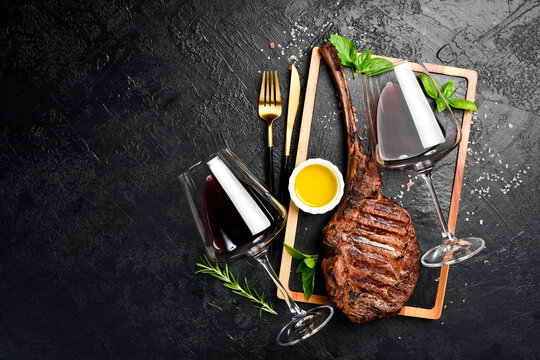 Wine in glasses and a juicy grilled steak on the bone. On a gray concrete background. Free space for text. Top view.