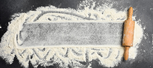 Baking background. flour and rolling pin on dark table with copy space, top view