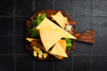 Cheese. Sliced ​​hard aged cheese and basil on a wooden cutting board.