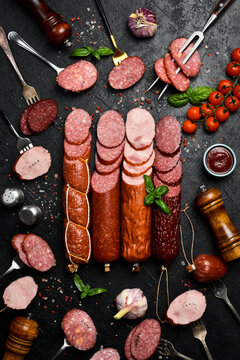 Assortment of different types of salami, paperoni and smoked sausages cut into slices on a dark stone table. Concrete background. Top view.