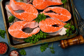 Set of fresh salmon or trout steaks with lemon, spices and parsley. Dark textured background.
