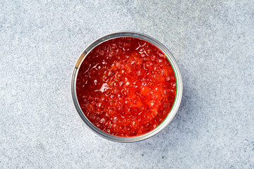 A jar of red salmon caviar. The products are rich in omega-3. Delicious seafood snacks. On a gray concrete background.