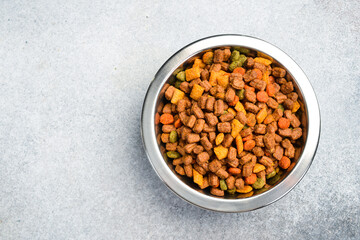Pet bowl with dry food on a gray textured background. Studio photo.