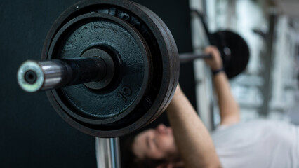 Close-up view of a barbell weight plate during a bench press in the gym, with a man lifting in the...