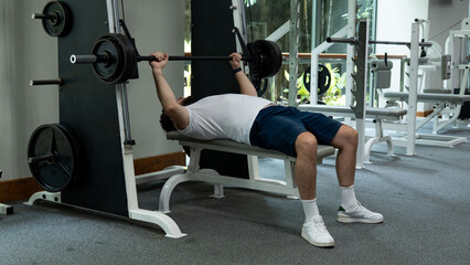 Man performing bench press with barbell on Smith machine in the gym, focusing on strength and chest...