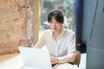 A woman is sitting at a table with a laptop in front of her. She is wearing a white shirt and has...