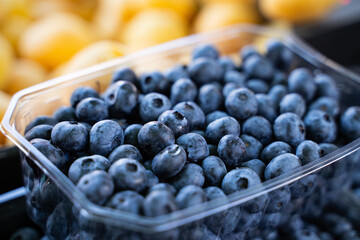 Close-up of blueberries in market containers on the grocery store stand, organic seasonal fruits displayed for sale, detail of colorful summer harvest, natural healthy food, side view